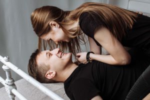 Mulher deitada em cima de um homem enquanto sorriem um para o outro.